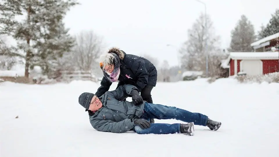 Äldre man halkat på snöig gata, får hjälp av dam. 