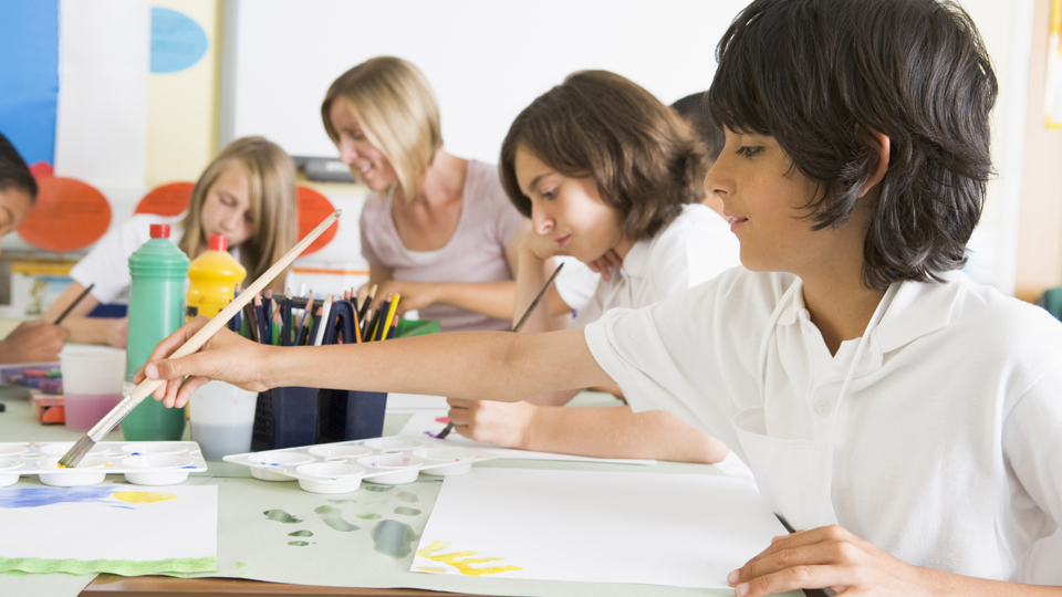Några barn målar med penslar på papper runt ett bord med en lärare.