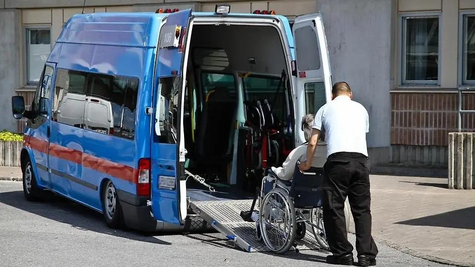 En person i rullstol som får hjälp in i en färdtjänstbil.