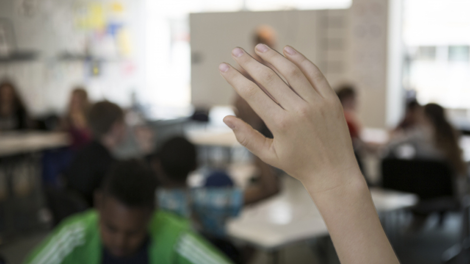 Hand som räcks upp i klassrum.