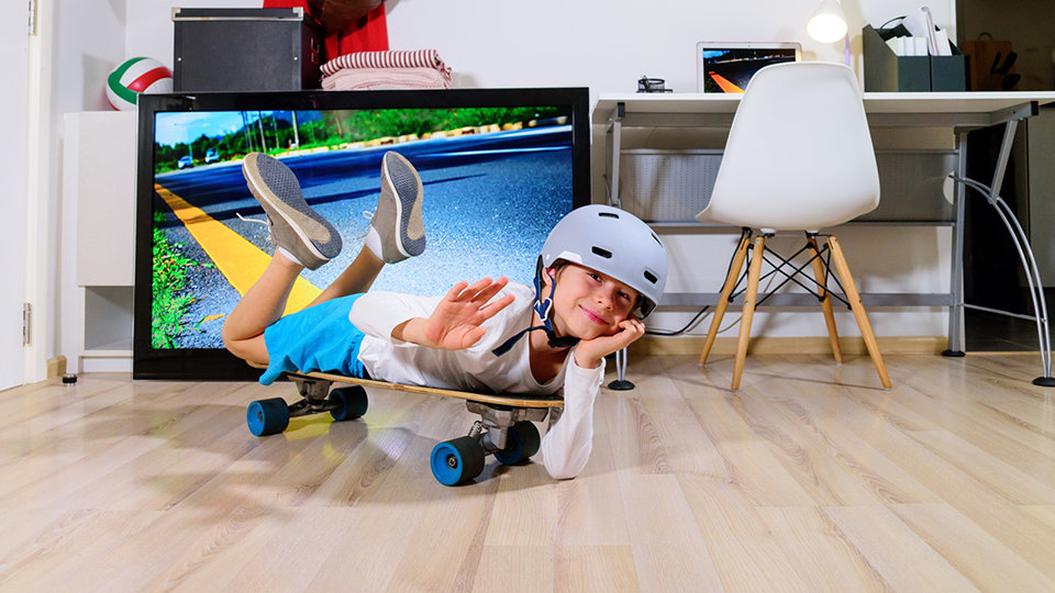 Pojke ligger på en skateboard inomhus med en TV i bakgrunden