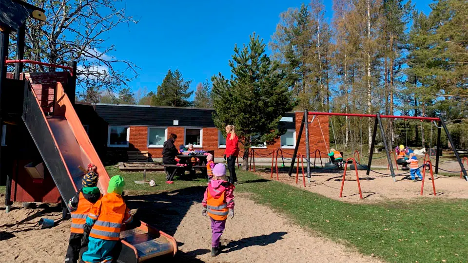 Barn leker på gården med pedagoger i bakgrunden.