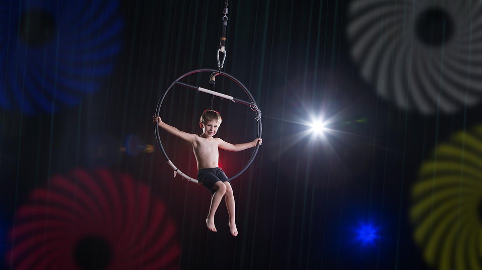 Ett barn sitter i en stor metallring som hänger högt upp i luften i en cirkusmanege.